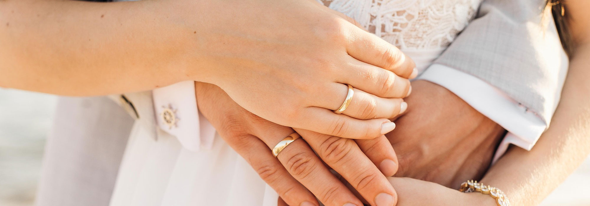 Hände mit goldenen Eheringen, überlappend, Teil von Hochzeitskleidung in Weiß und Grau